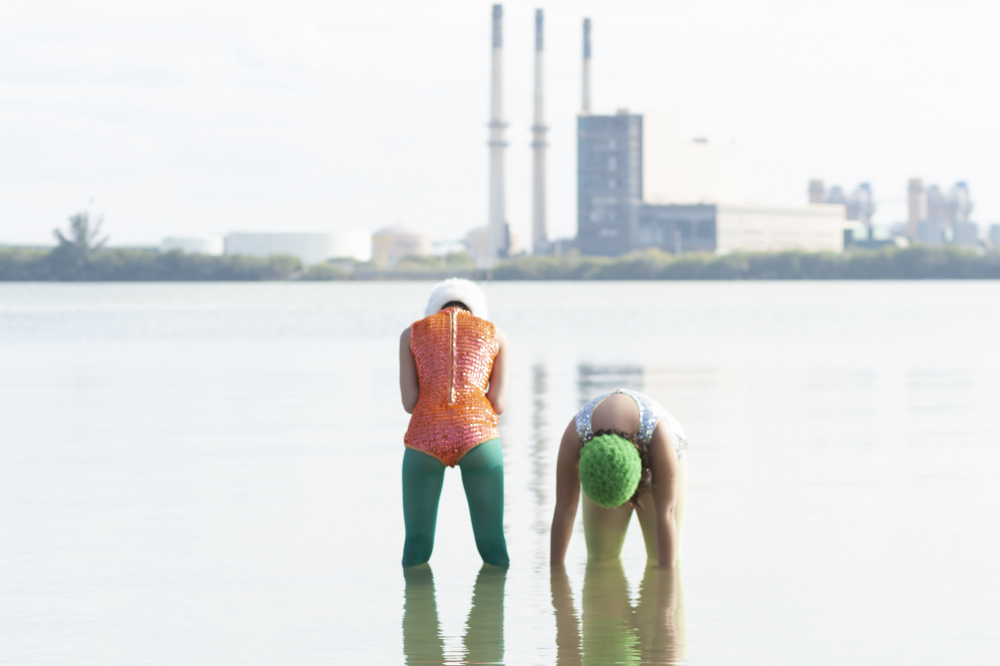 Two figures in colorful swimwear standing in shallow water