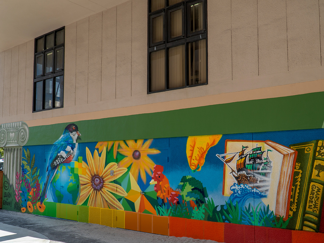 A colorful mural with a bird on a globe, vibrant flowers, geometric shapes, and an open book with a ship.