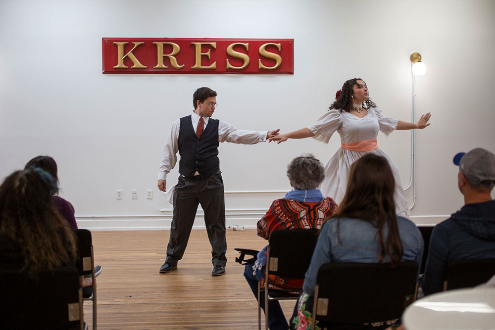 A man and woman perform a dance under a "KRESS" sign, with an audience seated in the foreground.