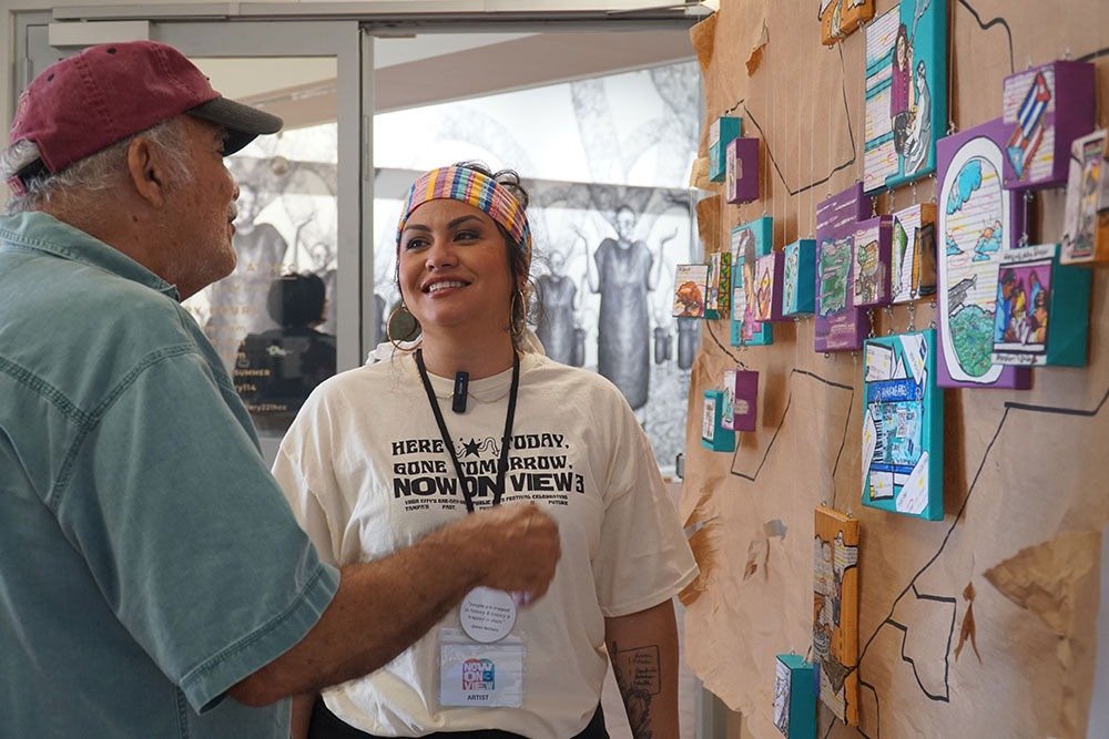 Two people converse in front of a colorful art display.