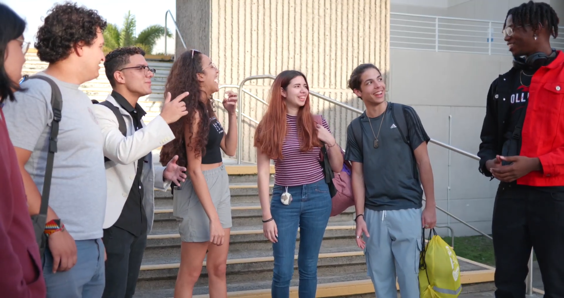 A group of six young people talking and laughing on an outdoor staircase.