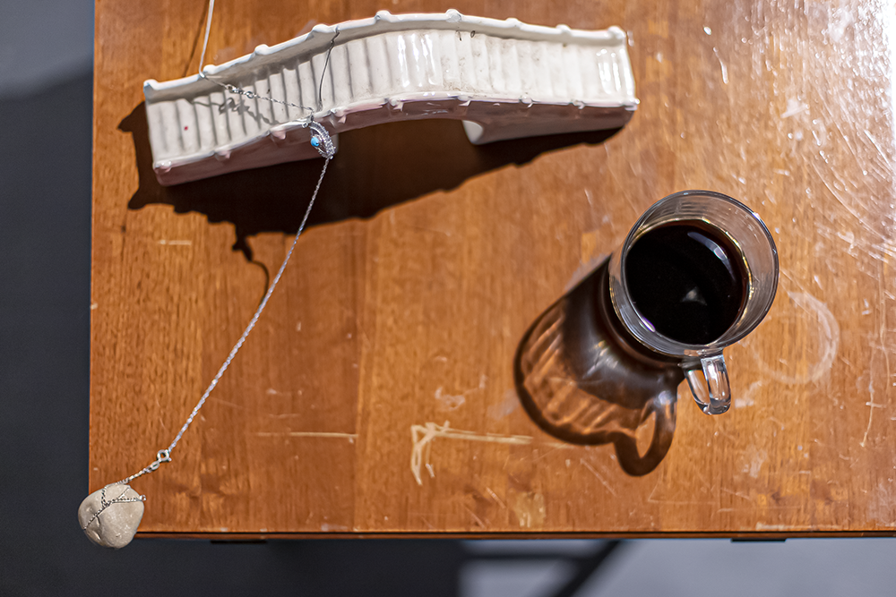 A glass cup of dark liquid and a ceramic bridge with a dangling stone on a wooden table.