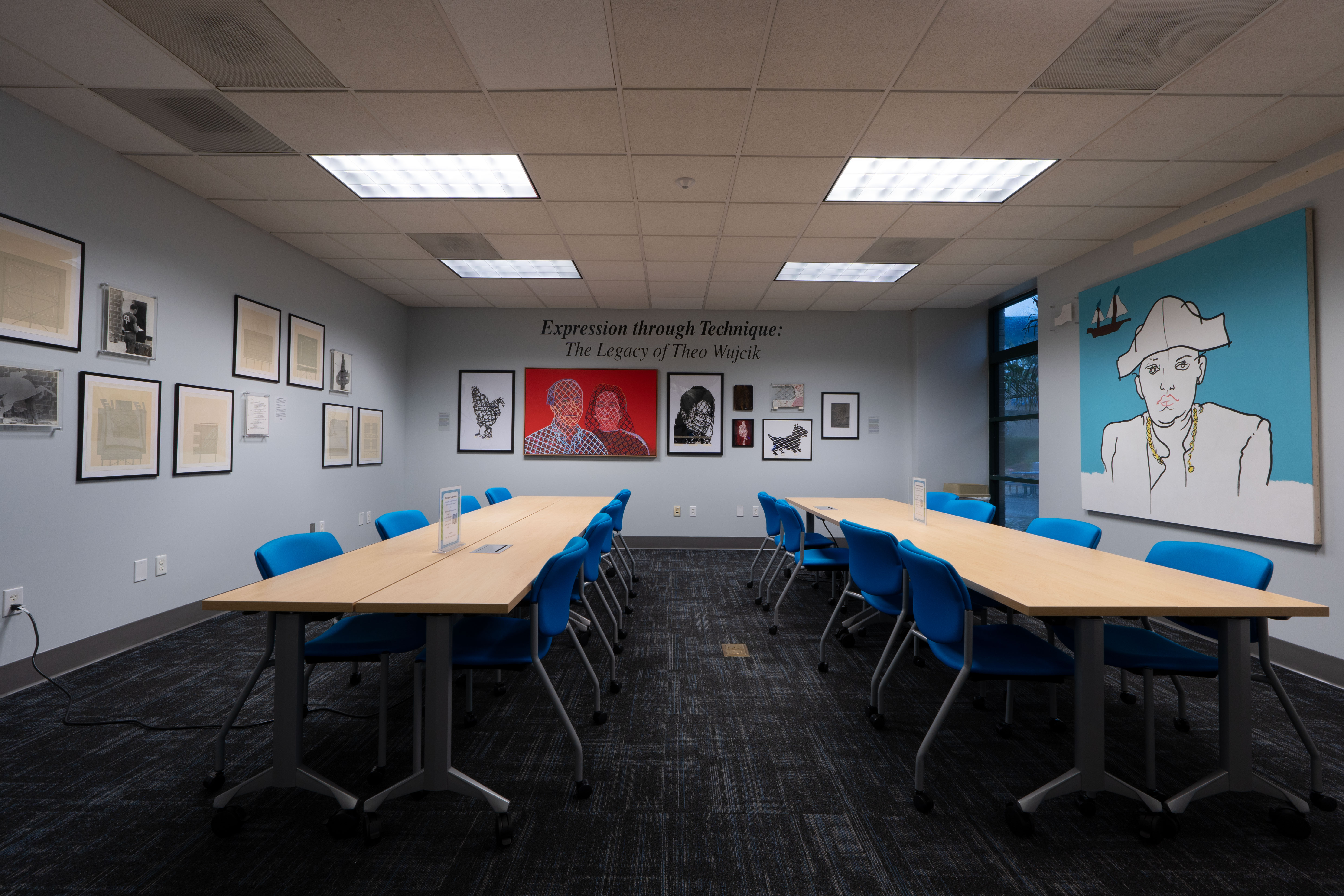 Conference room exhibition displaying artwork from Expression through Technique: The Legacy of Theo Wujcik, with framed pieces installed throughout the space.