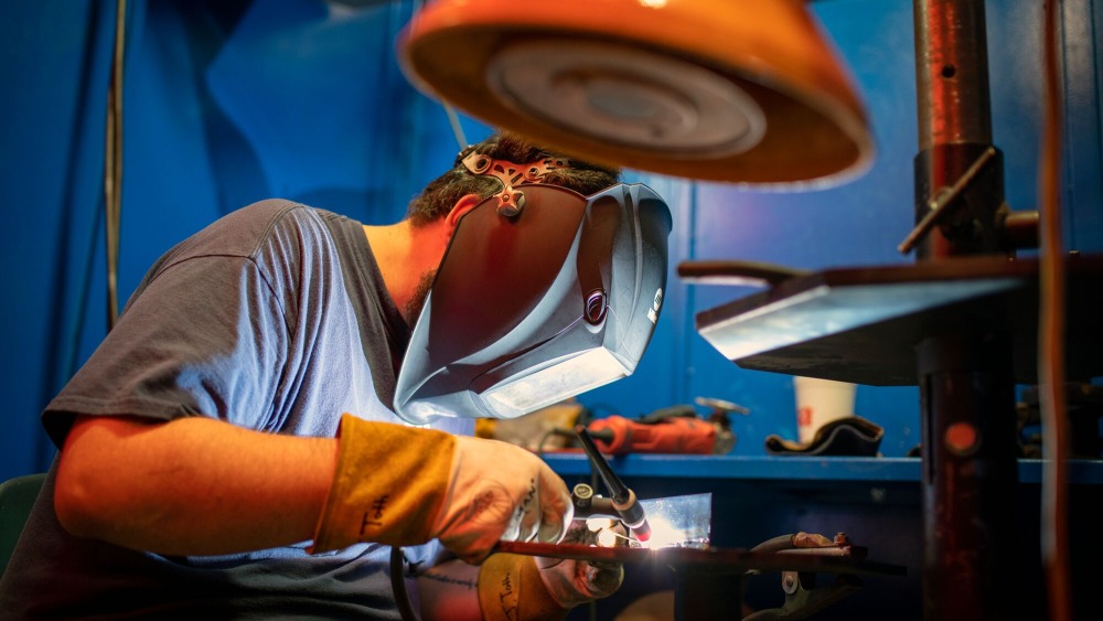 male welding student with welding mask on trying to weld some metal together