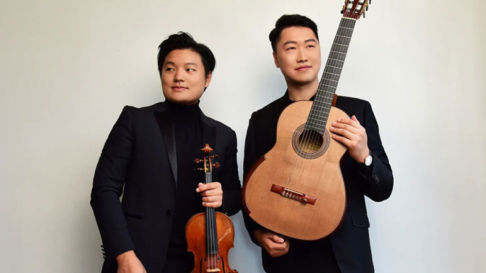 Two individuals in formal black attire, one holding a violin and the other a classical guitar.