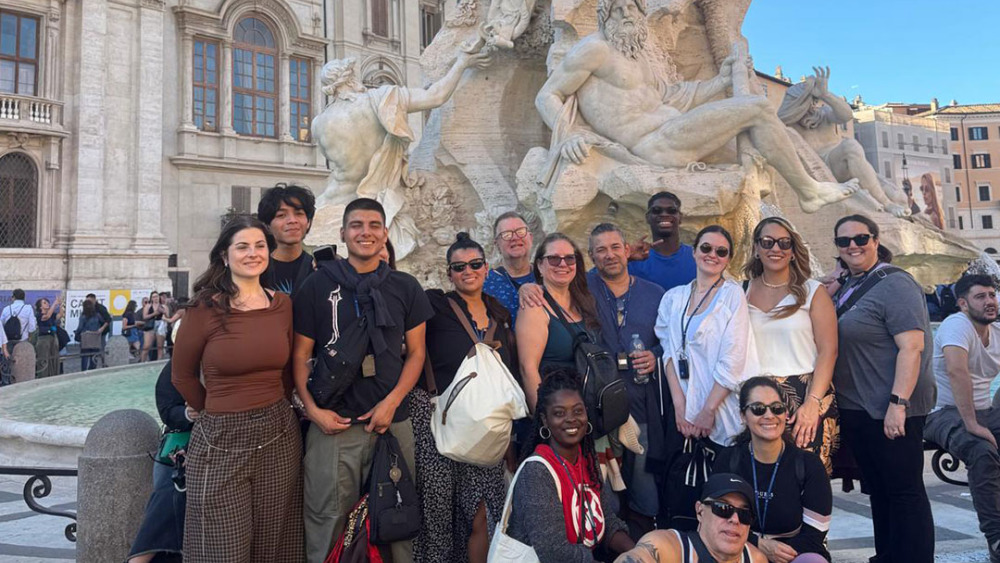 A group of people posing in front of an ornate fountain with sculptures.