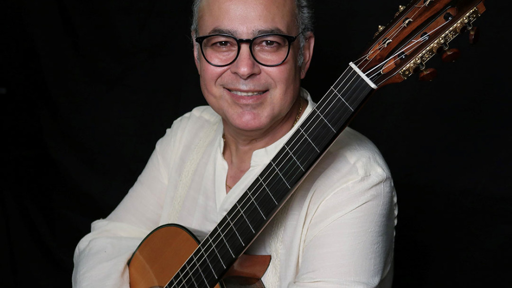 Rafael Martín Padrón smiling with a classical guitar against a dark background.