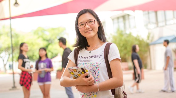 Student standing outside campus holding book.