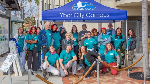 A group of people in teal shirts under a blue "Ybor City Campus" tent.