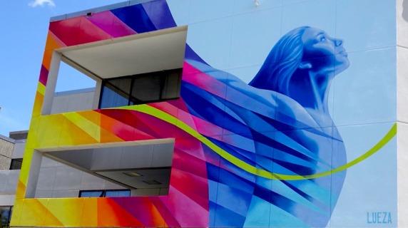 Colorful mural on a building, combining geometric patterns and a blue figure gazing upwards.