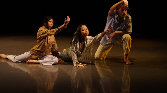 Three dancers pose dynamically on a dimly lit stage.