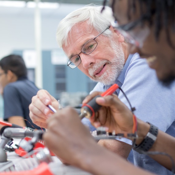 Engineering male students in a classroom welding wires and circuits