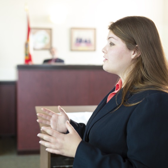 Criminology female student in a courtroom speaking to the jury that is offscreen