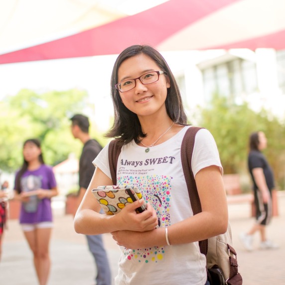 Student standing outside campus holding book.