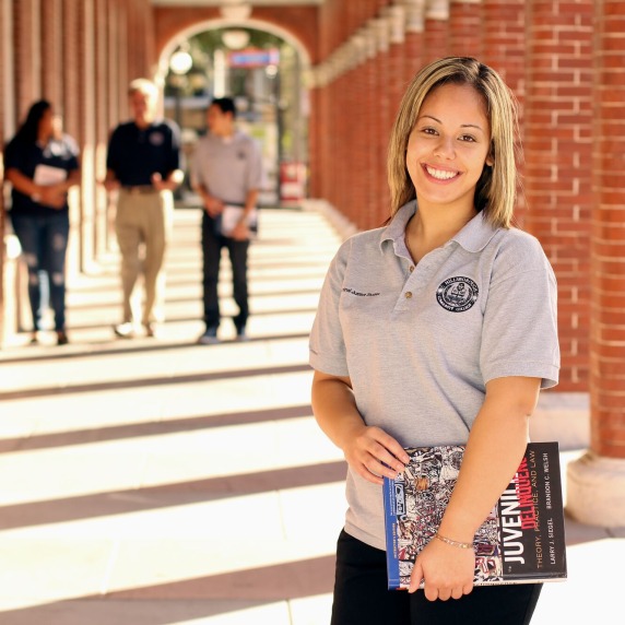 Female student holding criminology textbook and smiling at camera.