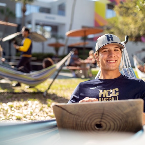 Male student sitting in a hammock with a laptop in his lap. 