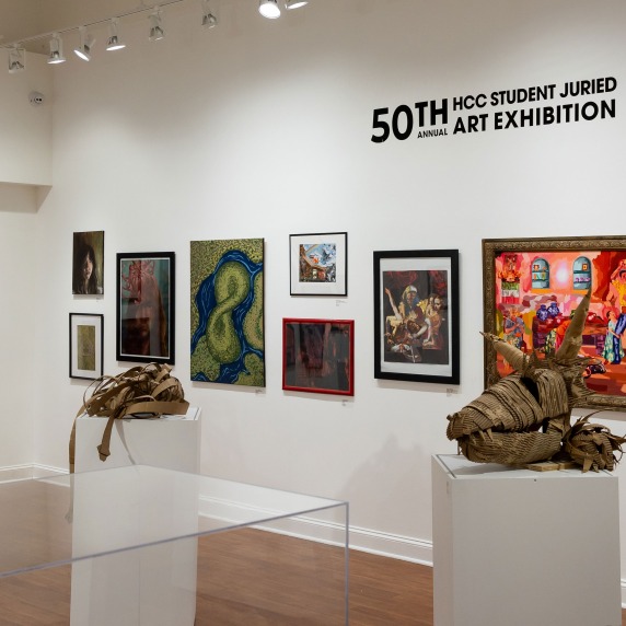 Gallery with various artworks on display, including paintings and sculptures, under bright track lighting.