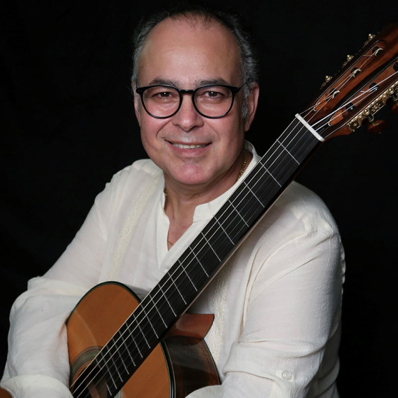 Rafael Martín Padrón smiling with a classical guitar against a dark background.