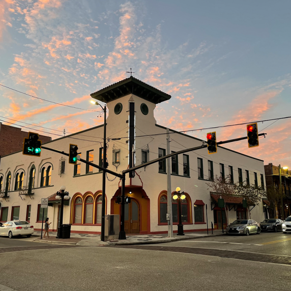 Historic white building with tower at sunset, traffic lights, and parked cars.