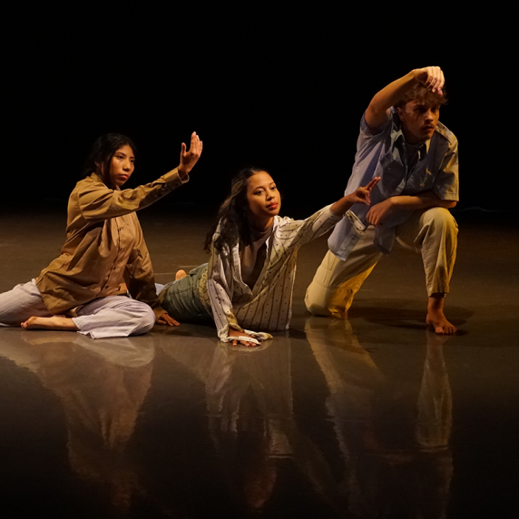 Three dancers pose dynamically on a dimly lit stage.