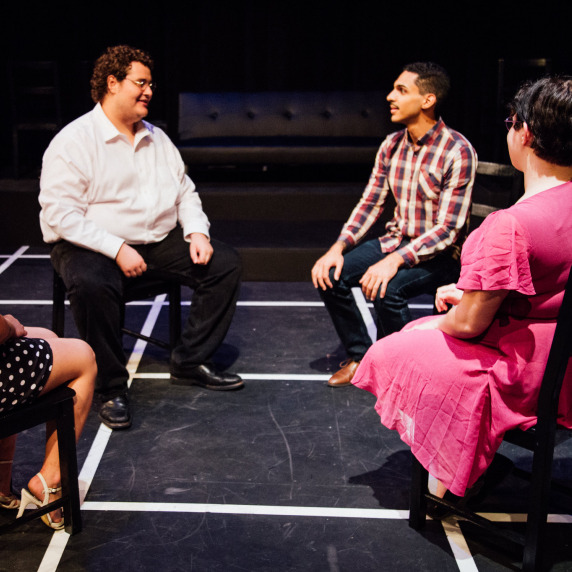 Four participants seated in a circle on a theater stage having a discussion.
