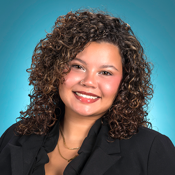 A woman with curly hair smiles into the camera while wearing a black blazer. 