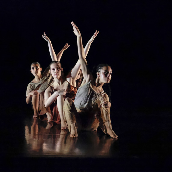 Dancers performing in a contemporary dance piece on a darkened stage.