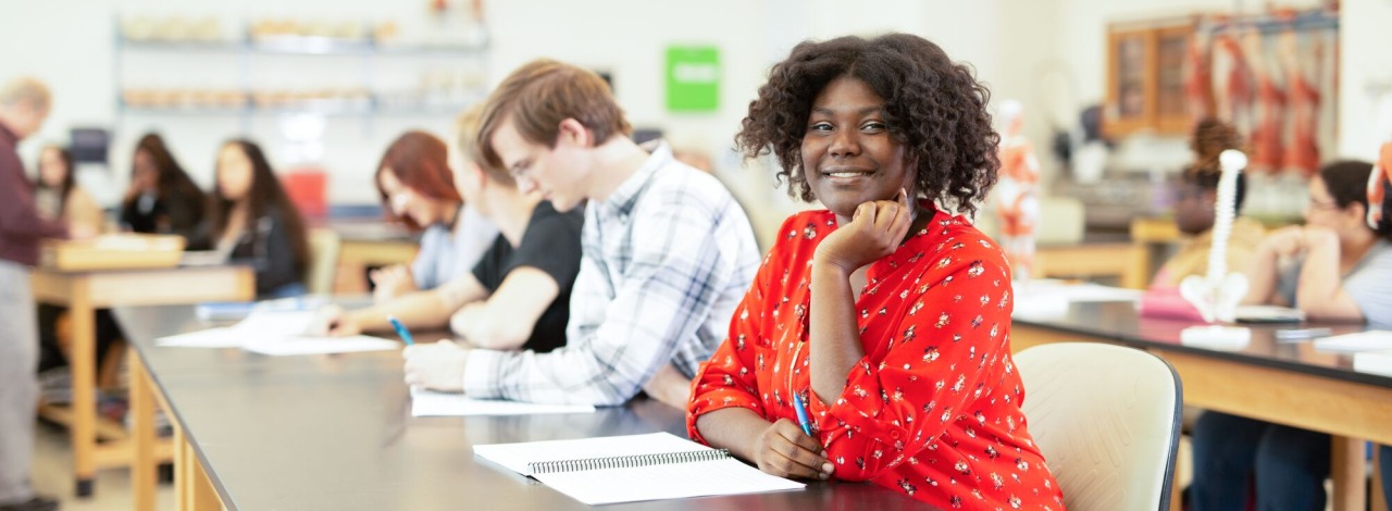 Woman in red shirt sitting at desk with other students in background