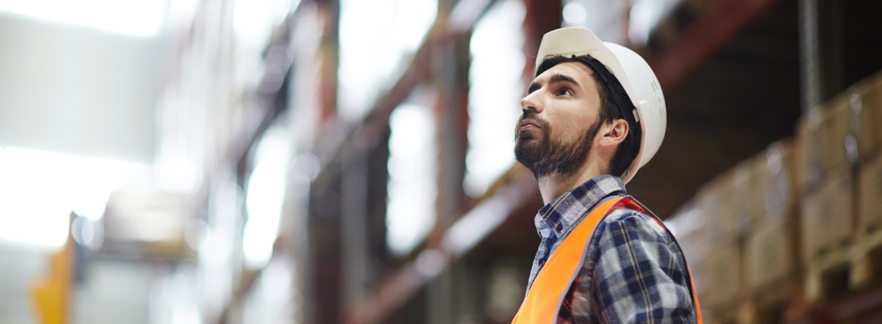 Man with touchpad looking up at stockpiles of merchandise.