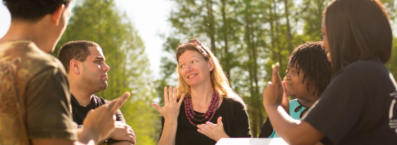 An instructor and students gathered around a table outside communicating in sign language