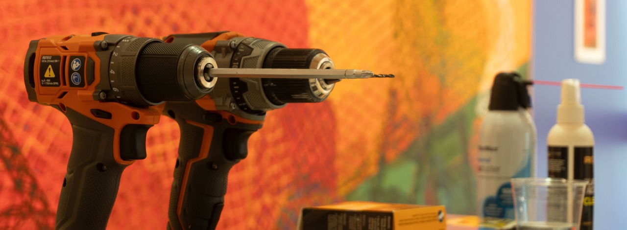 Two orange and black cordless drills on a table with boxes and bottles in a colorful background.