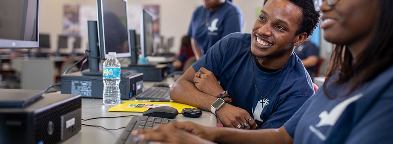 Two people working at computers in a room, both wearing blue shirts with a logo.