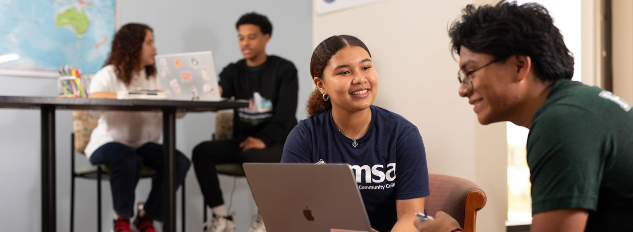 A group of three students collaborate on schoolwork in a study space, with a world map on the wall and a sign reading "HONORS" above.