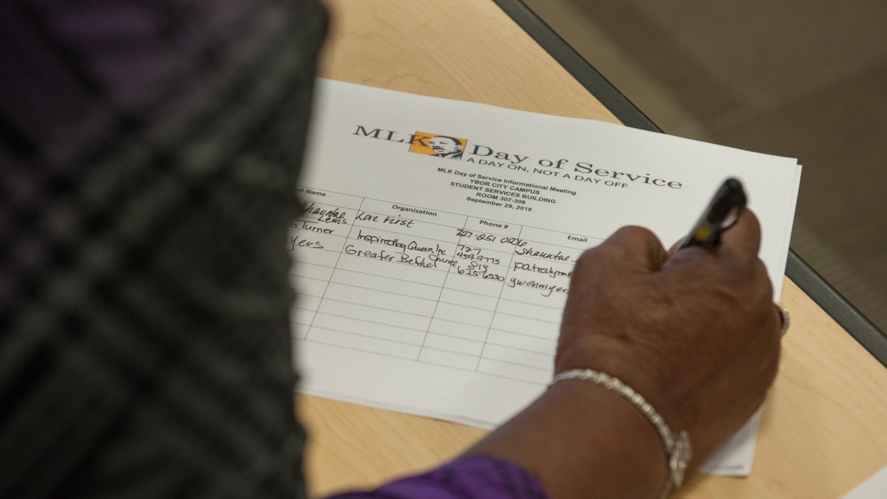 Person's hand filling out a sign-in sheet for MLK Day of Service informational meeting