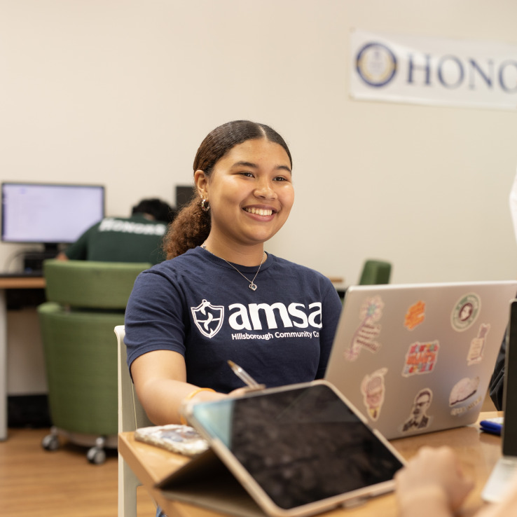 Female student sitting at a desk and working on a laptop while smiling. 