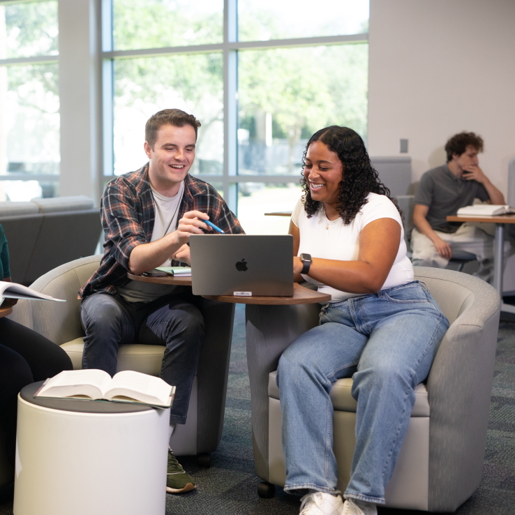 Student sitting in a library and engaging with a laptop. 